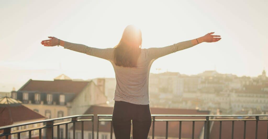 Woman standing with arms out facing towards the sunshine for Vitamin D Exposure